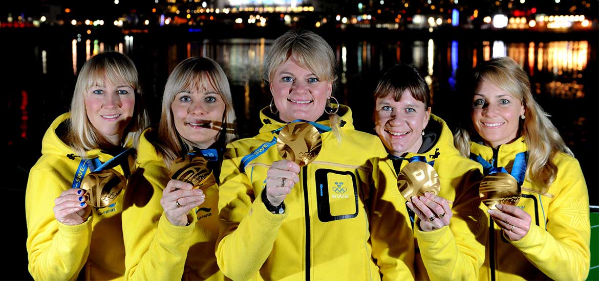 Lag Anette Norberg i gula jackor och guldmedaljer runt halsen.