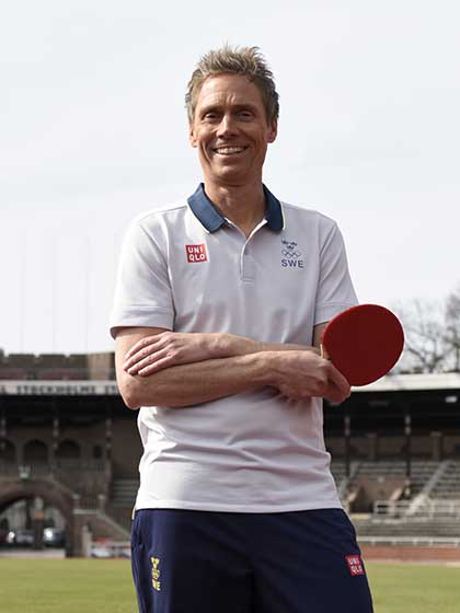 En blond man ler mot kameran och håller ett pingisracket i handen. 