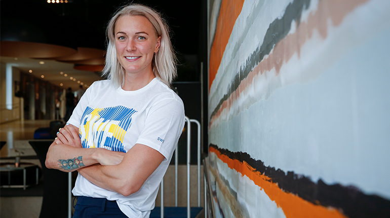 Simmaren Sarah Sjöström blont hår står vänd åt sidan med blicken in i kameran. Hon har på sig en tröja som det står SWE på.
